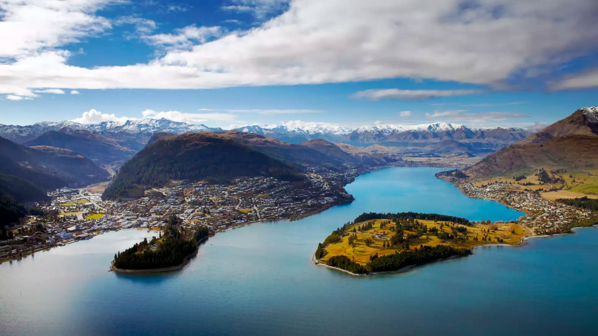 Aerial view of Queenstown and Frankton around a lake with mountains and partly cloudy sky