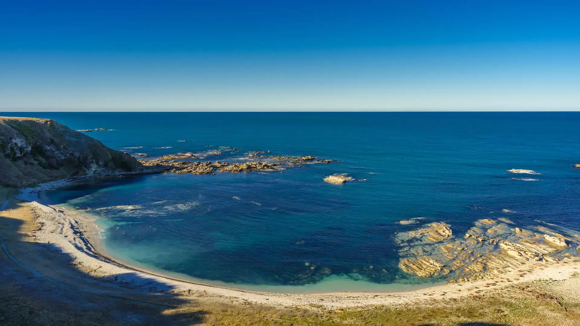 Clear blue ocean and rocky beach forming a curved bay under sunny blue sky.