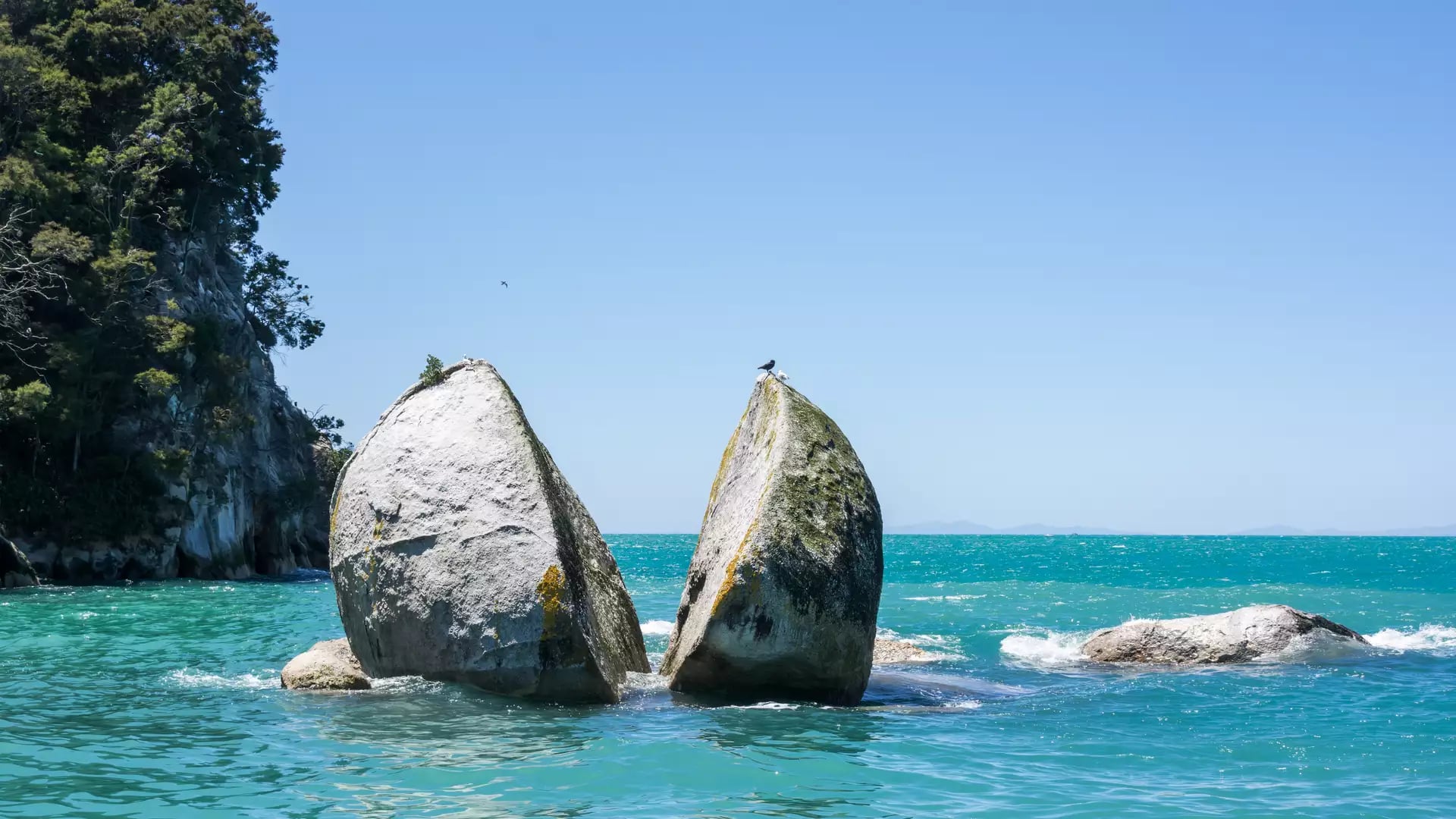A giant circular granite rock split in two sitting in bright turquoise water.
