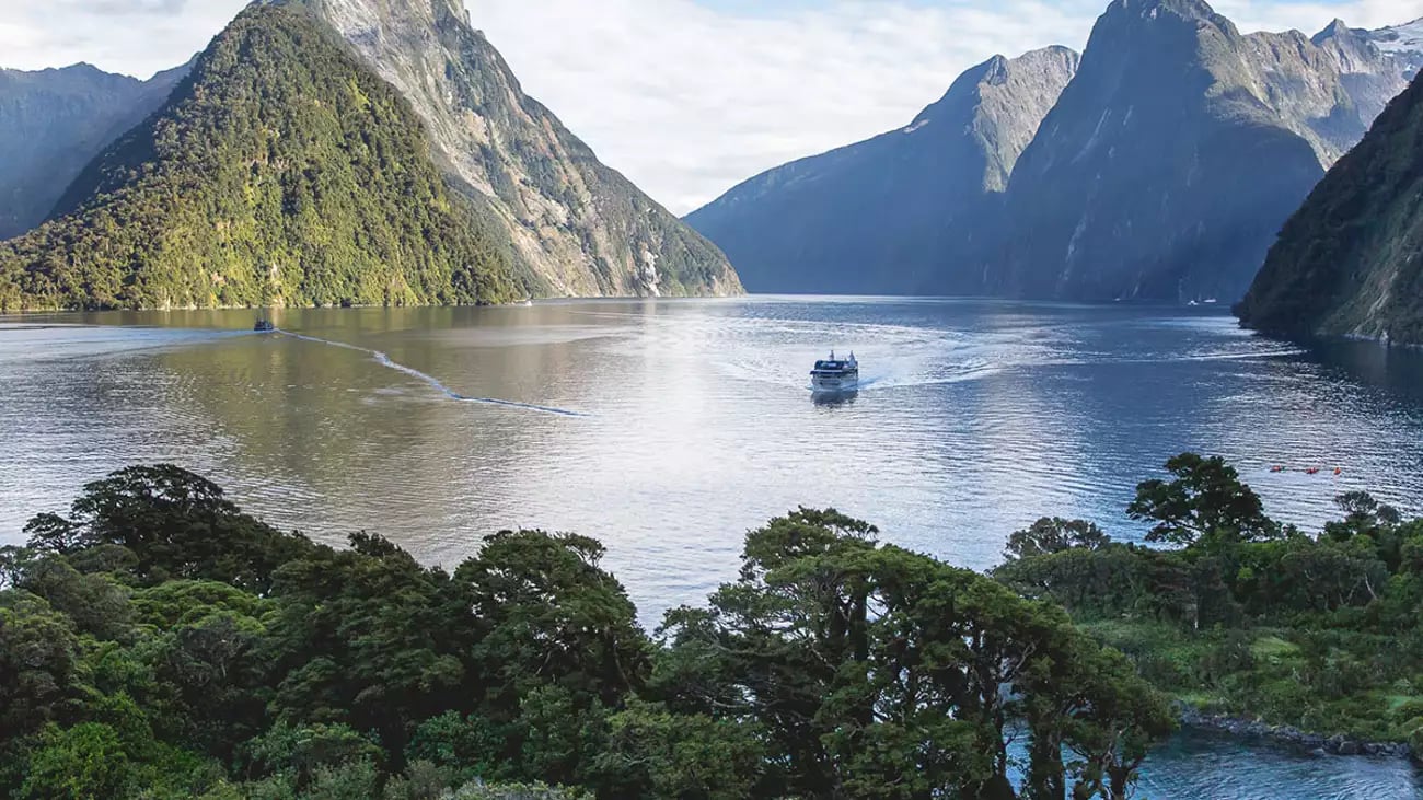 Milford Sound with a cruise boat, surrounded by mountains and lush greenery.