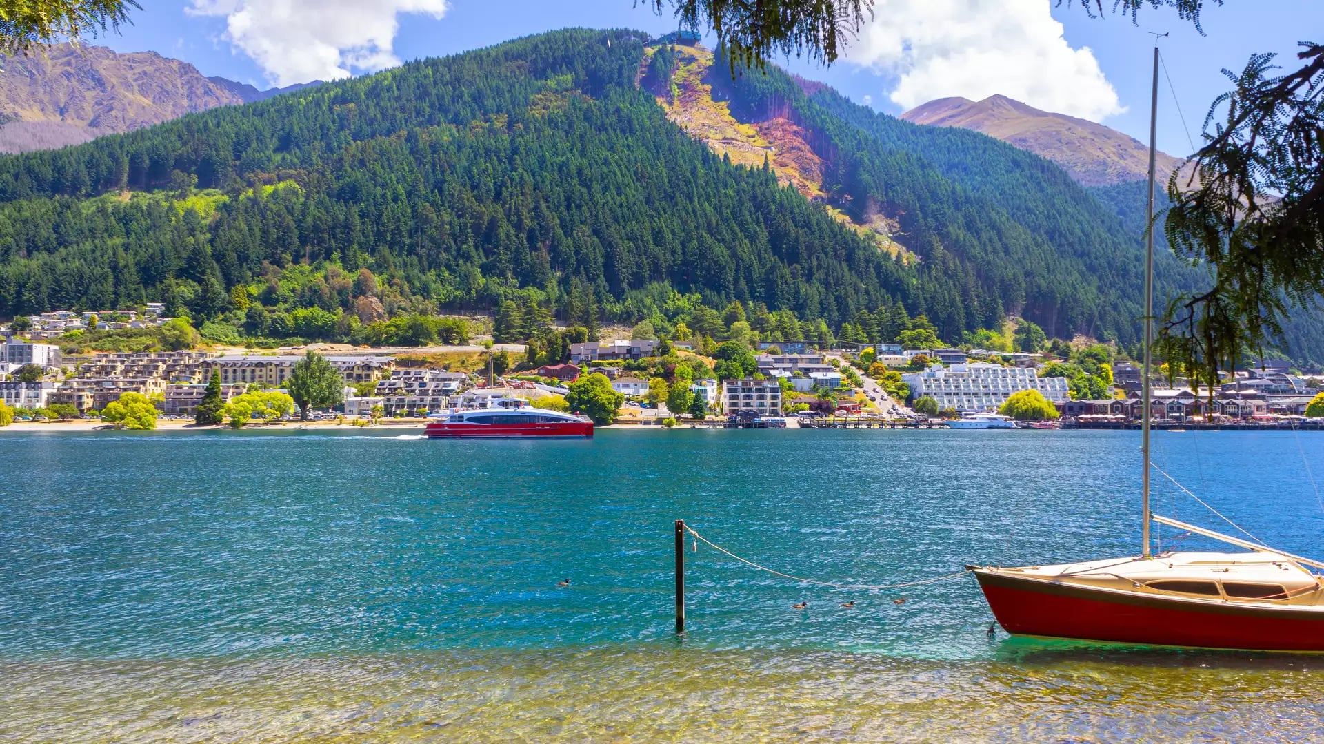 Looking out over Lake Wakatipu in Queenstown with a green hill and boats on the lake 