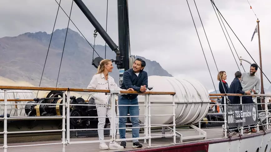Travelers on TSS Earnslaw steamboat with mountains.