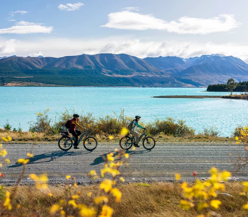 People biking beside lake and mountains in Lake Tekapo
