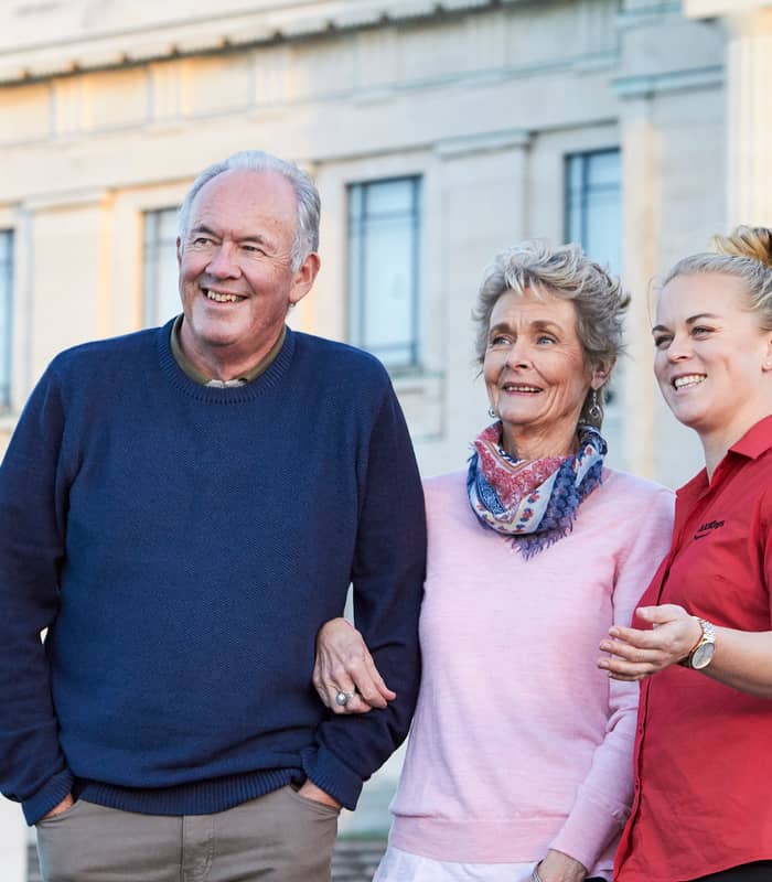 Senior couple with a tour guide standing outside a historic building in Auckland.