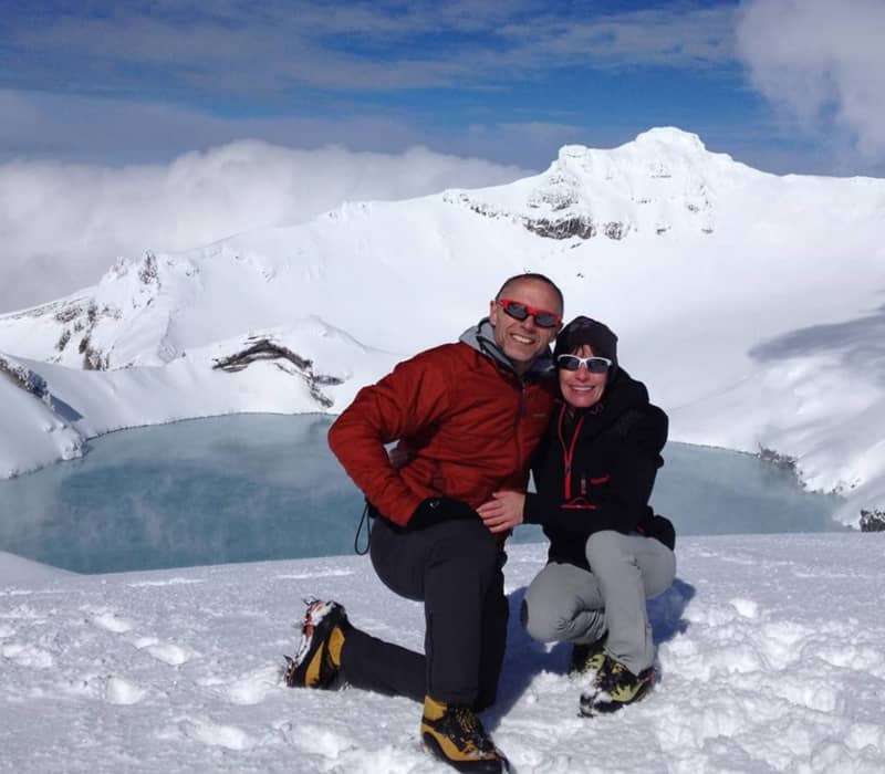 Hikers posing at the snowy summit of a volcano overlooking a turquoise crater lake.