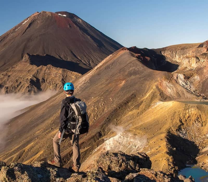 Hiker with blue helmet overlooking volcanic Red Crater and lakes under clear blue sky