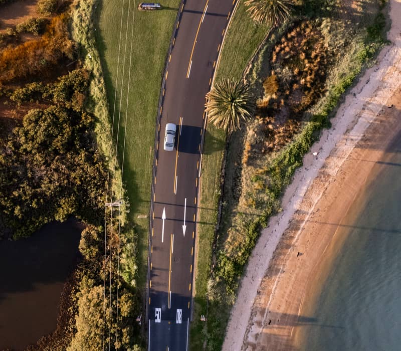 Aerial view of a curved coastal road beside a beach in the Bay of Islands.