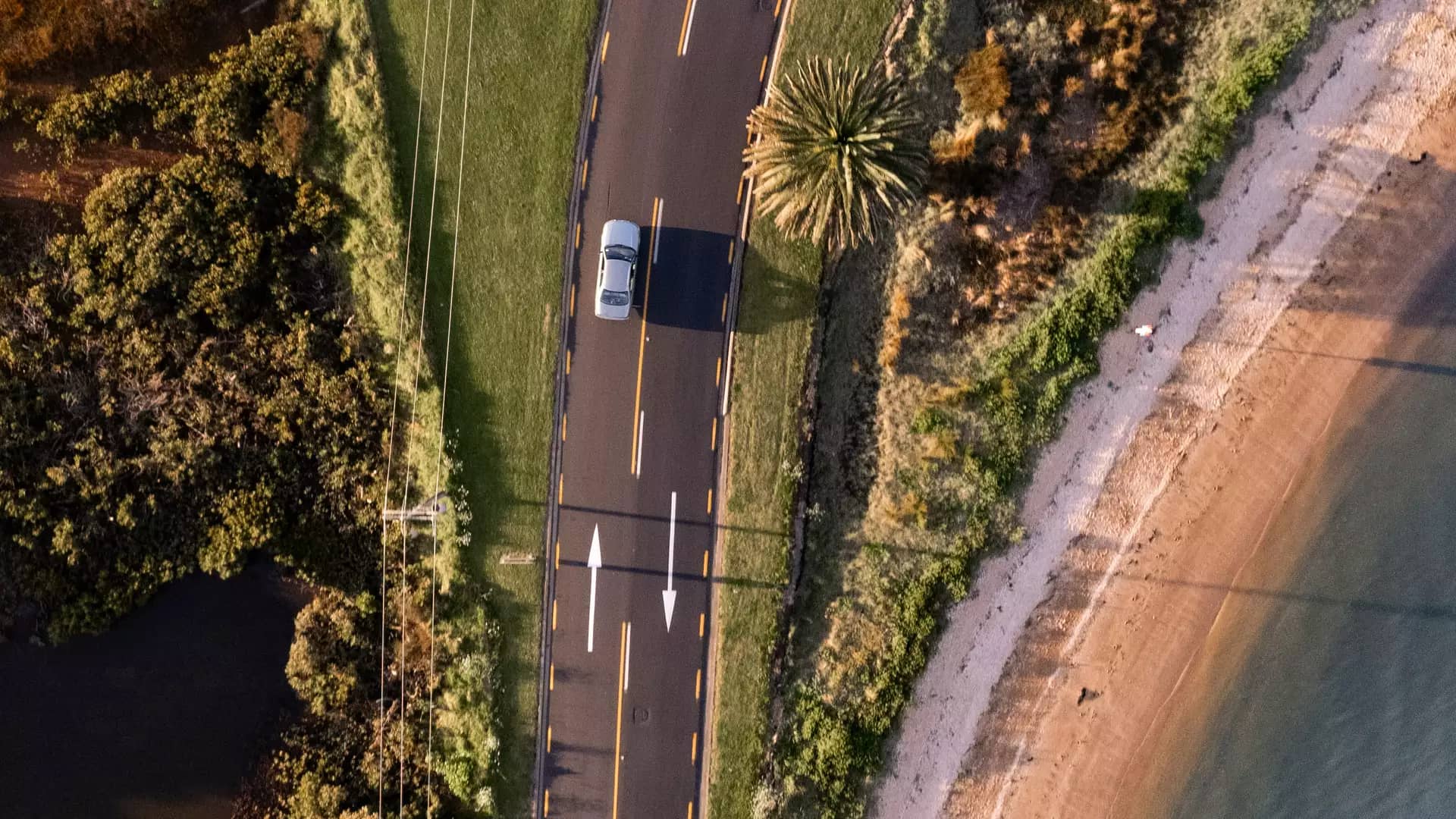 Aerial view of a curved coastal road beside a beach in the Bay of Islands.