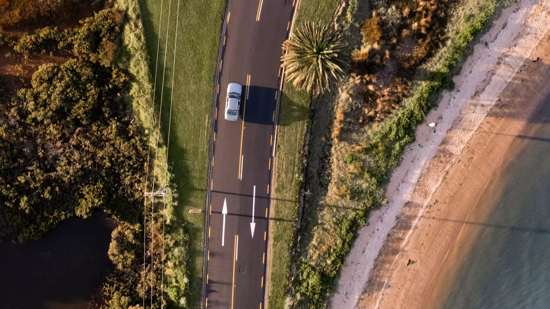 Aerial view of a curved coastal road beside a beach in the Bay of Islands.