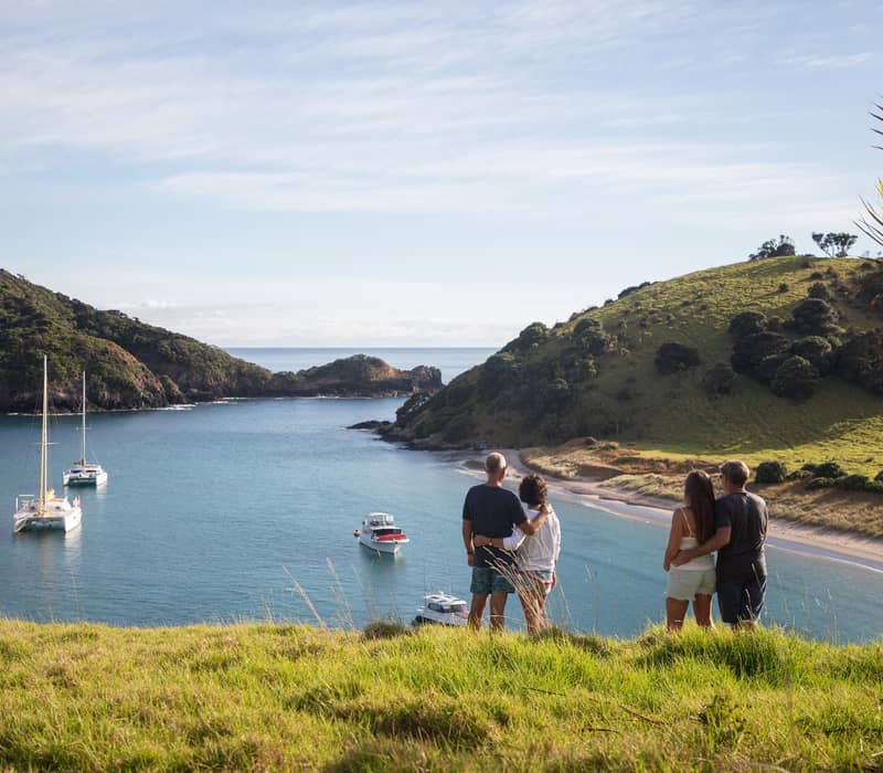 Couples overlooking a calm bay with boats and green hills in the Bay of Islands.