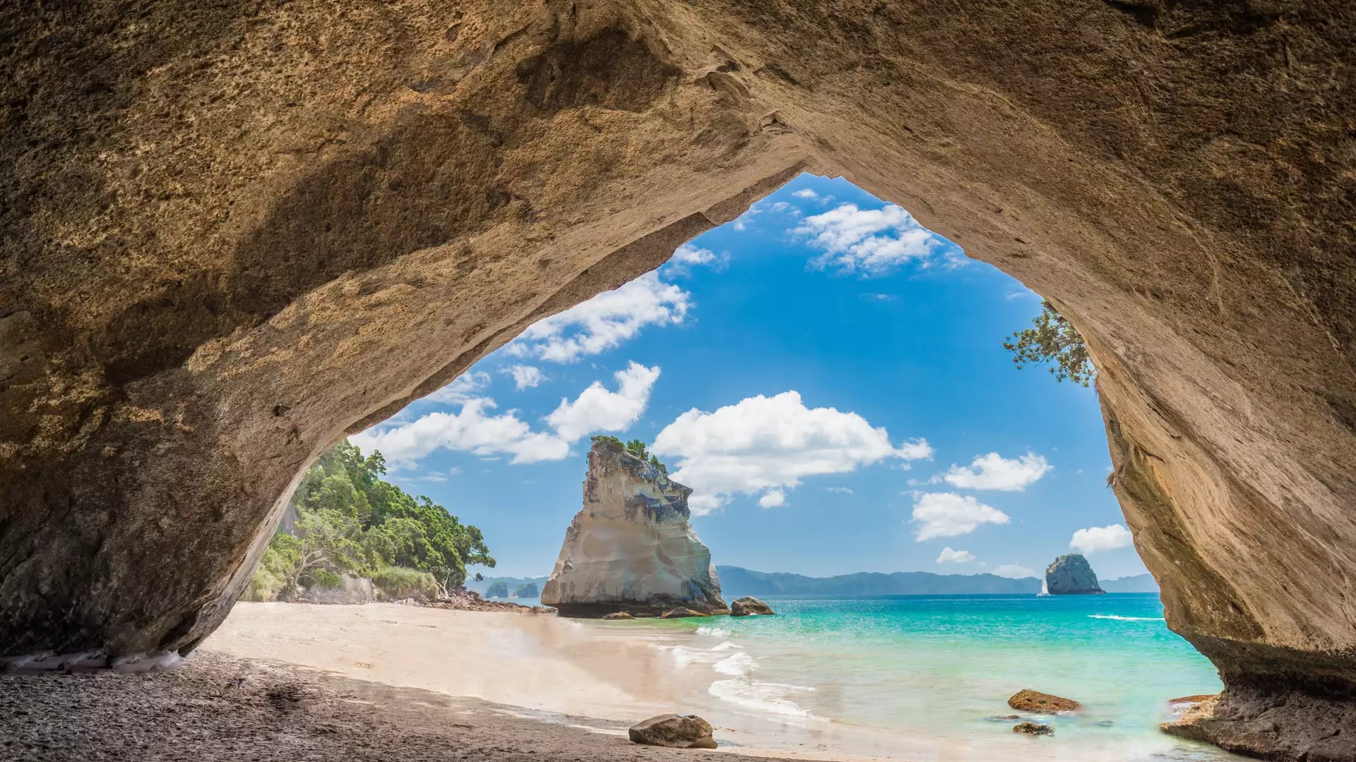 View of sandy beach and ocean seen through a large natural rock arch with sea stacks and blue sky