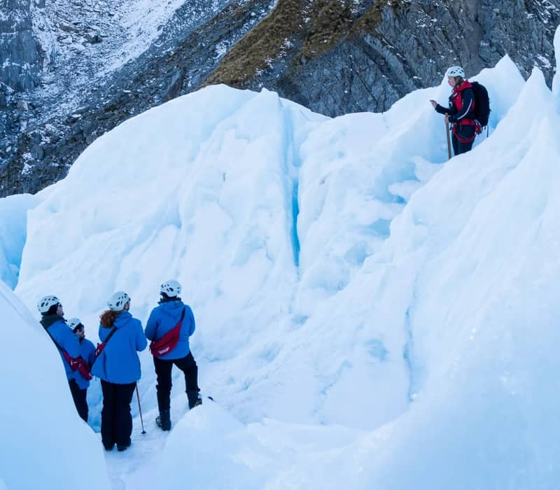 Group of people ice trekking with guide on Franz Josef Glacier snowy and icy terrain.