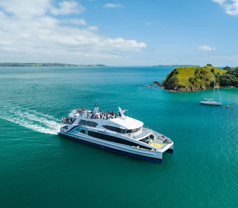 Ferry boat with passengers on blue water near green hilly island and small sailboat.