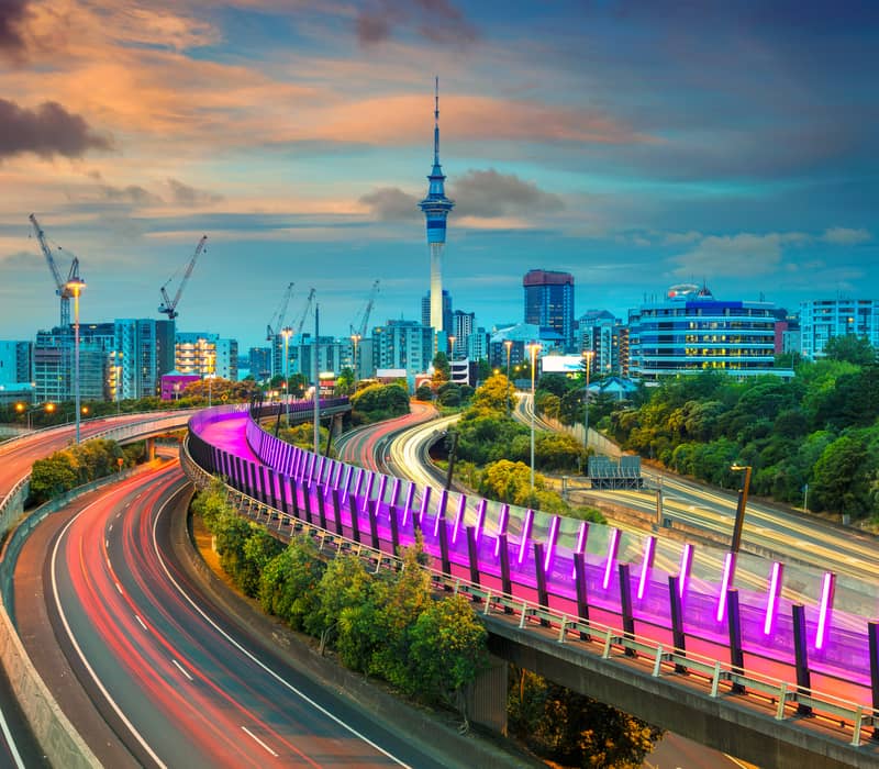 Auckland city skyline at sunset with Skytower and light trails on curved highways.