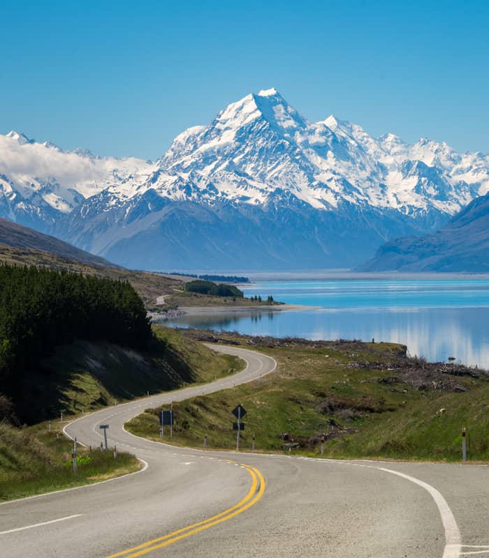 Winding road beside a lake with snow-covered mountains in the background on a clear day
