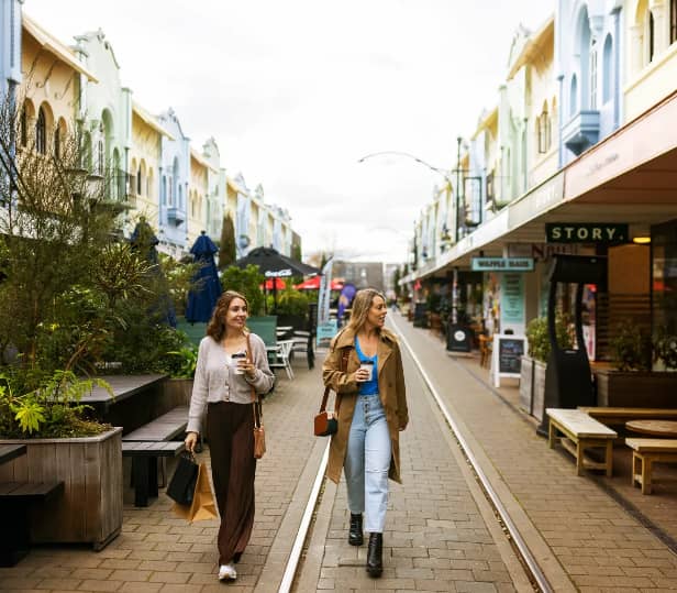 Two women walking down a pedestrian street with coffee and shopping bags in Christchurch.
