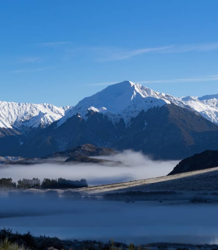 Snowy mountain peaks with mist over a lake and blue sky above in a peaceful valley.