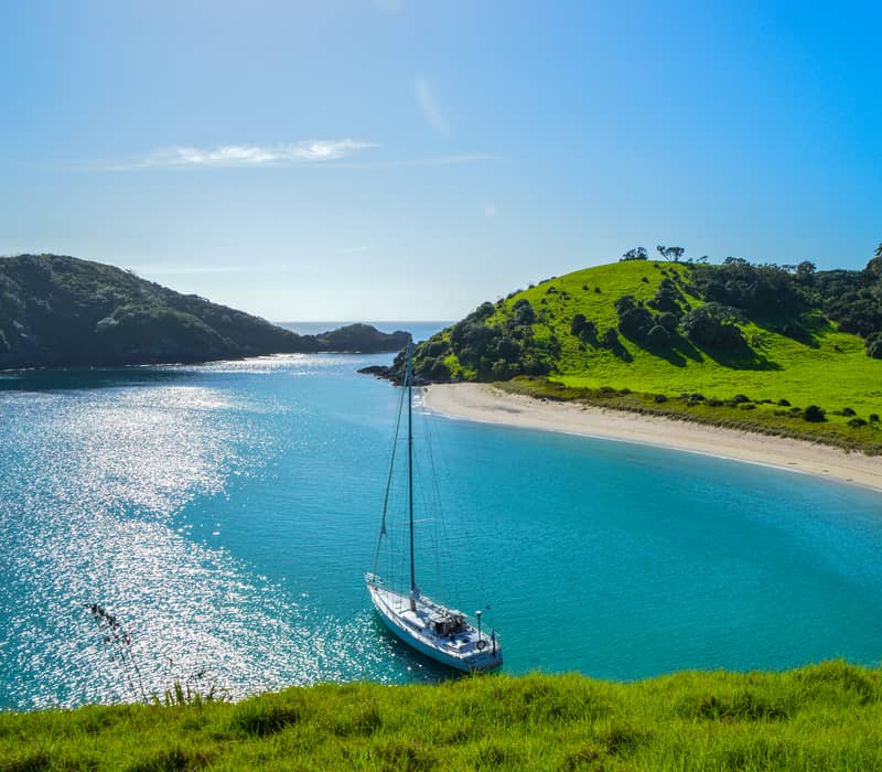 Sailboat anchored in turquoise bay with green hills and sandy beach on a sunny day