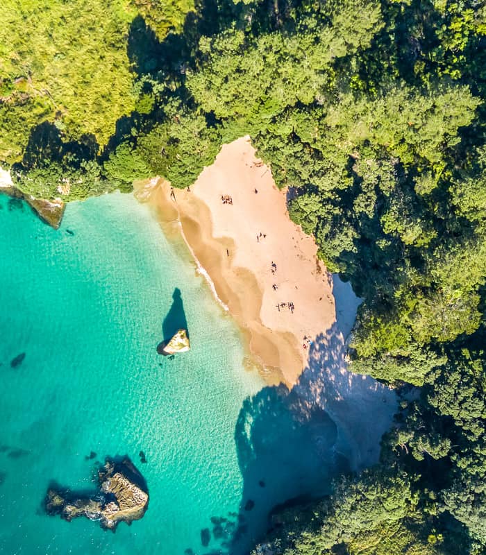Aerial view of a turquoise beach surrounded by dense green forest and rocky coastline.