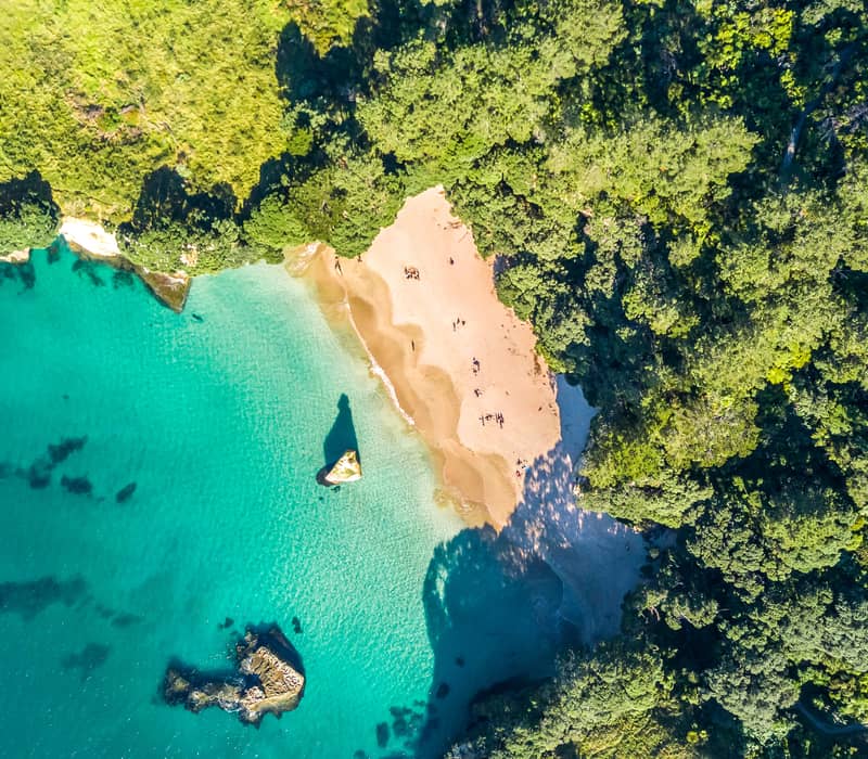 Aerial view of a turquoise beach surrounded by dense green forest and rocky coastline.