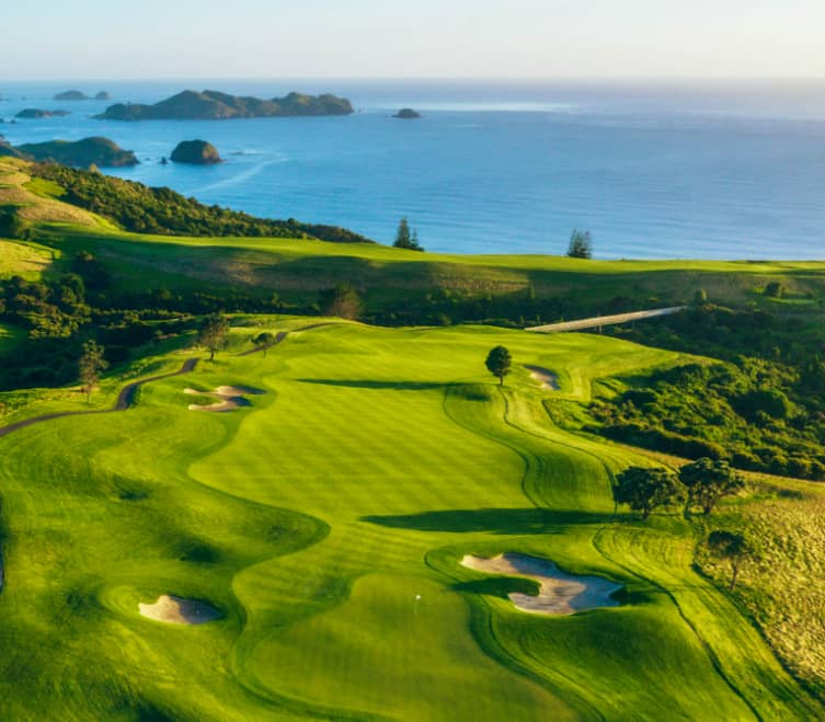 An aerial view of the vibrant green fairways and white sand bunkers at Kauri Cliffs golf course overlooking the Pacific Ocean.