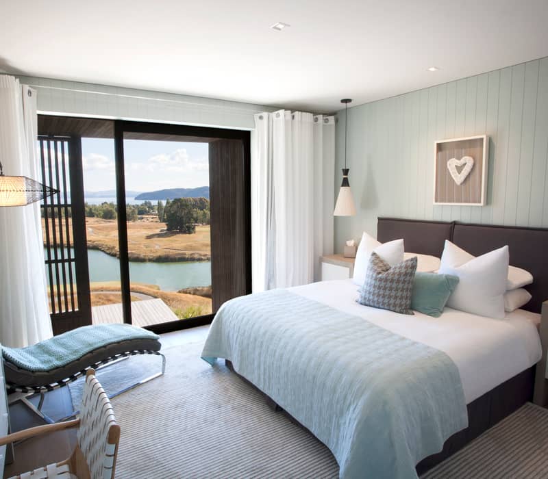Modern bedroom suite with blue bedding and river view through glass doors