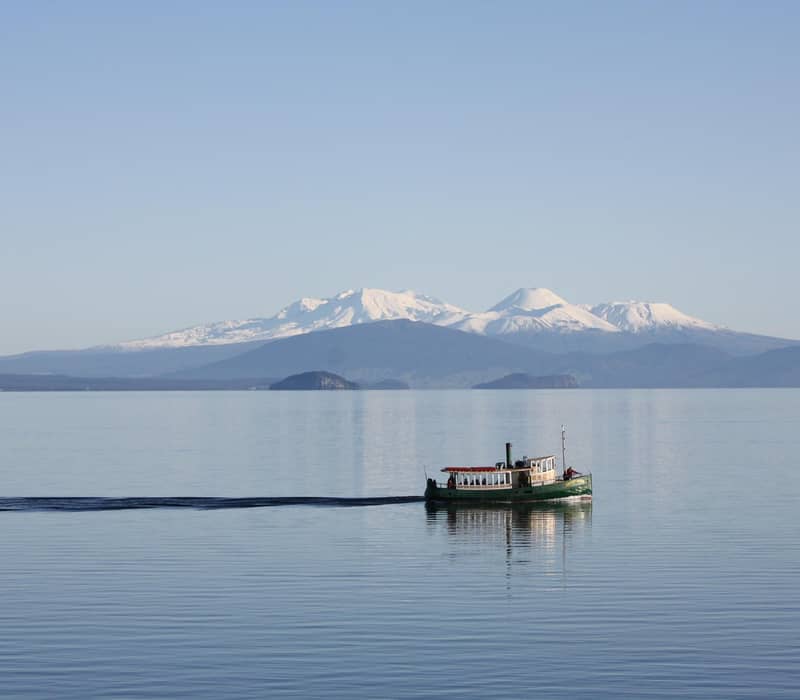 Boat cruising on Lake Taupo with snowy mountain in backdrop.