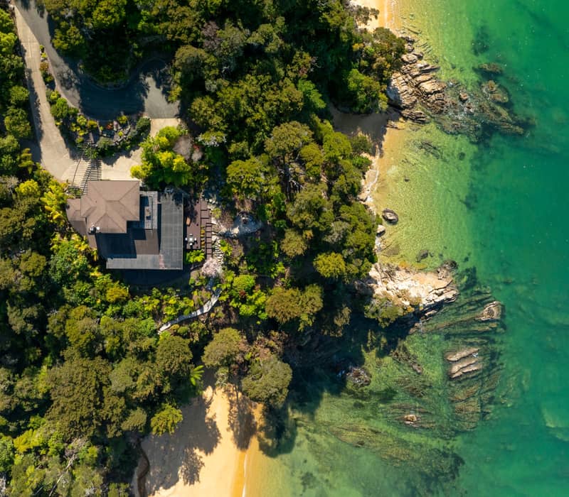 Aerial shot of the luxury lodge sitting on the cliff by the turquoise waters of the abel tasman.