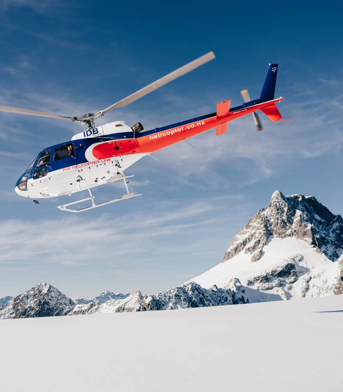 Helicopter flying over snowy mountain peak under blue sky.