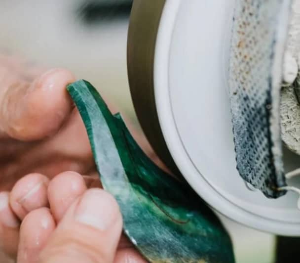 Hands polishing a green jade stone on a grinding wheel.