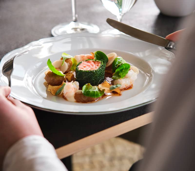 Close-up of gourmet seafood dish with salmon and shrimp on white plate at a dining table.
