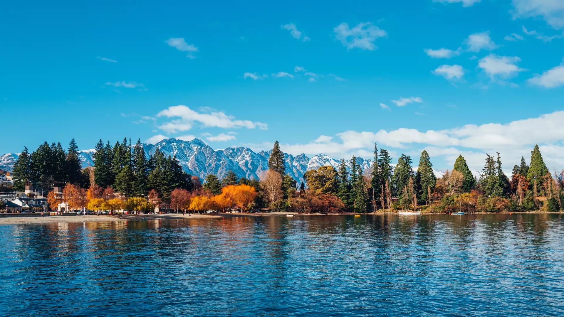 Autumn trees and snow-capped mountains reflected in lake water at Queenstown.
