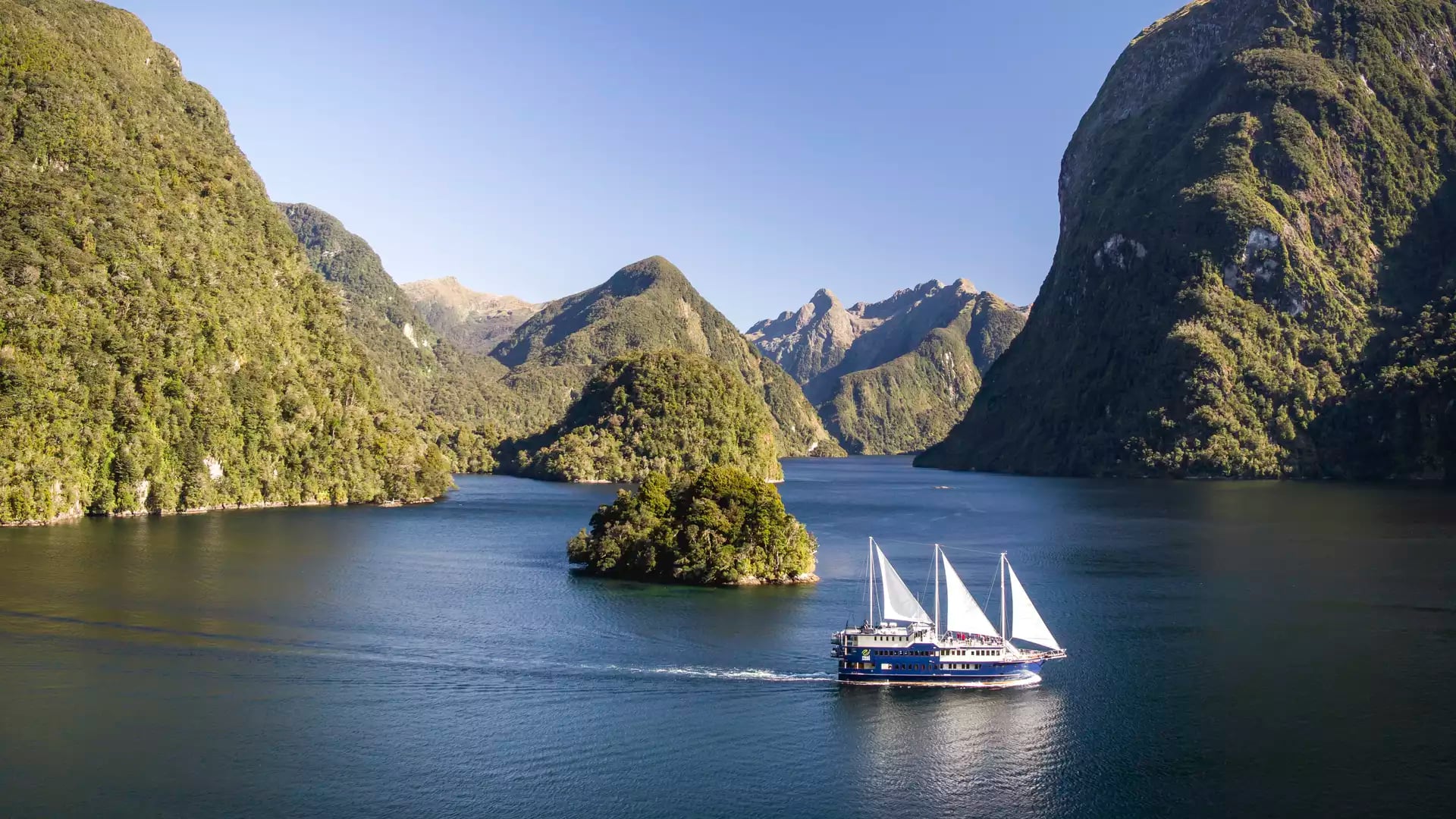 Cruise boat sailing in forested fjord with mountains and clear blue sky