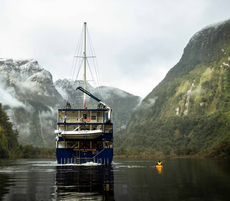 Cruise ship in fjord surrounded by foggy mountains and kayak on calm water