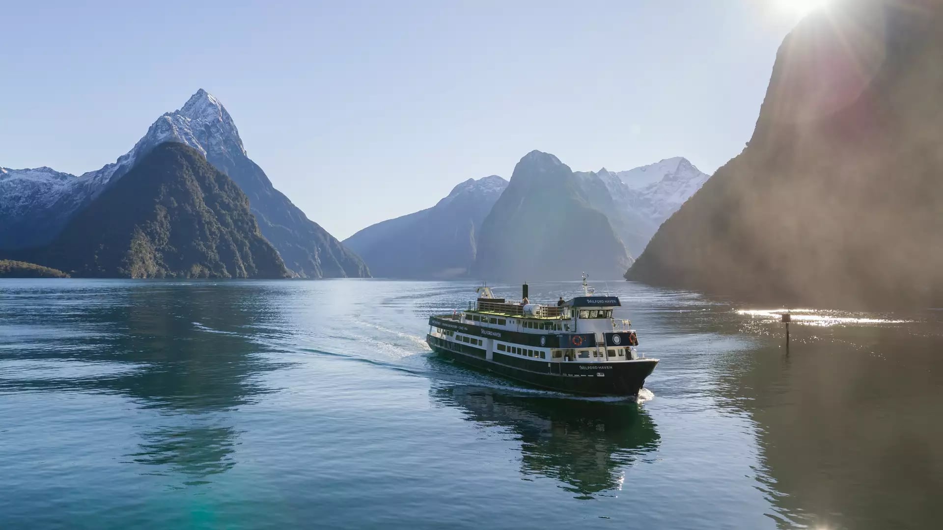 Milford Mariner cruise ship sails in misty fjord surrounded by tall mountains and cloudy skies.