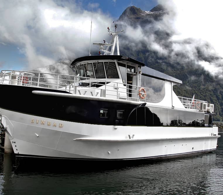 Sinbad ferry boat docked at Milford Sound with mountains and clouds in the background.