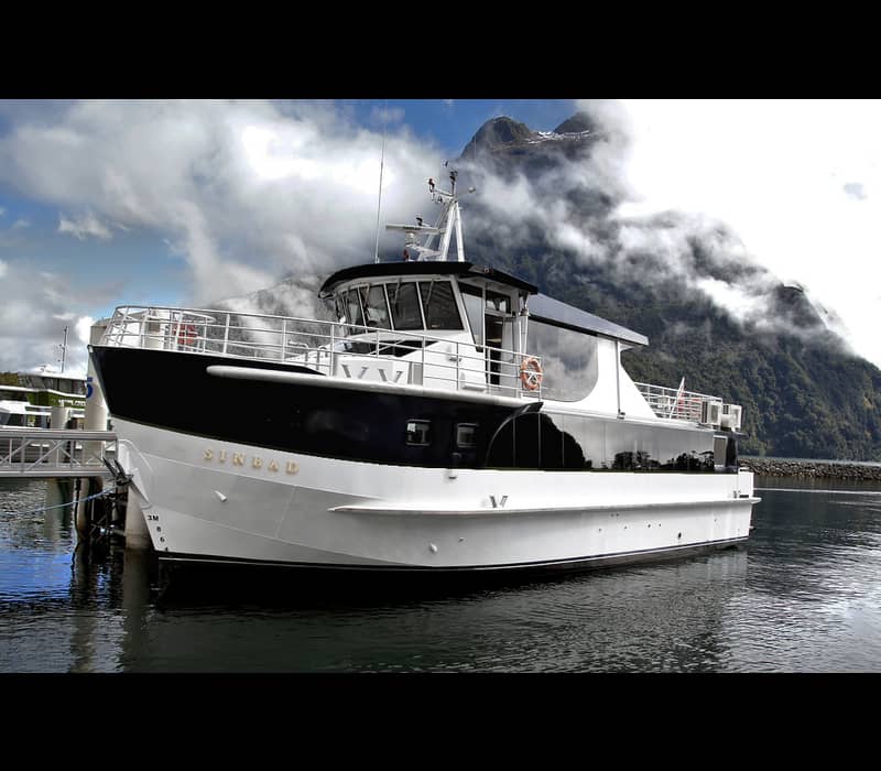 Sinbad ferry boat docked at Milford Sound with mountains and clouds in the background.