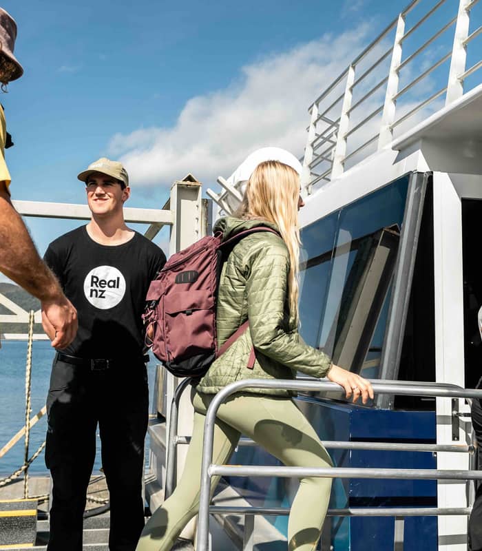 People with backpacks boarding a boat at dock on a sunny day with partly cloudy sky.