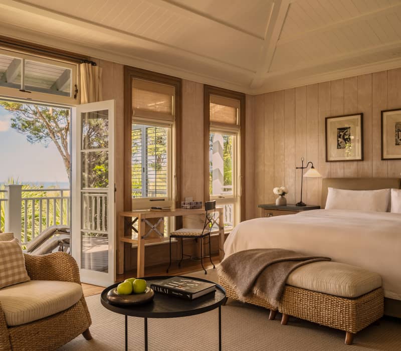 Junior suite bedroom with large bed, armchair, desk, and open balcony doors showing ocean view.