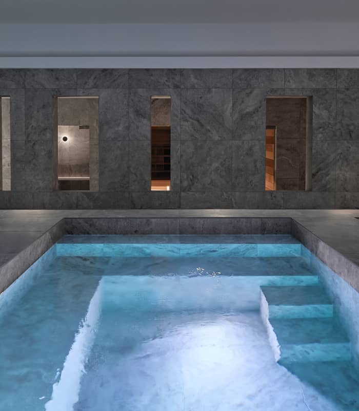 Modern indoor thermal bathhouse in Queenstown with hot and cold plunge pools surrounded by grey travertine stone walls.