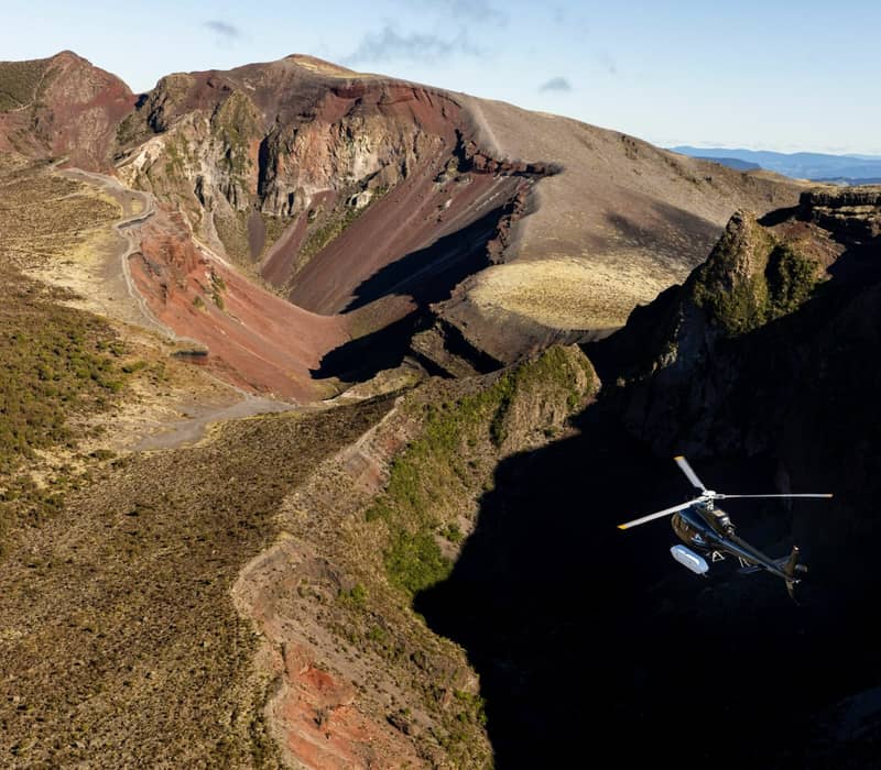 Helicopter flying over the volcanic crater of Mount Tarawera with rocky terrain and clear sky