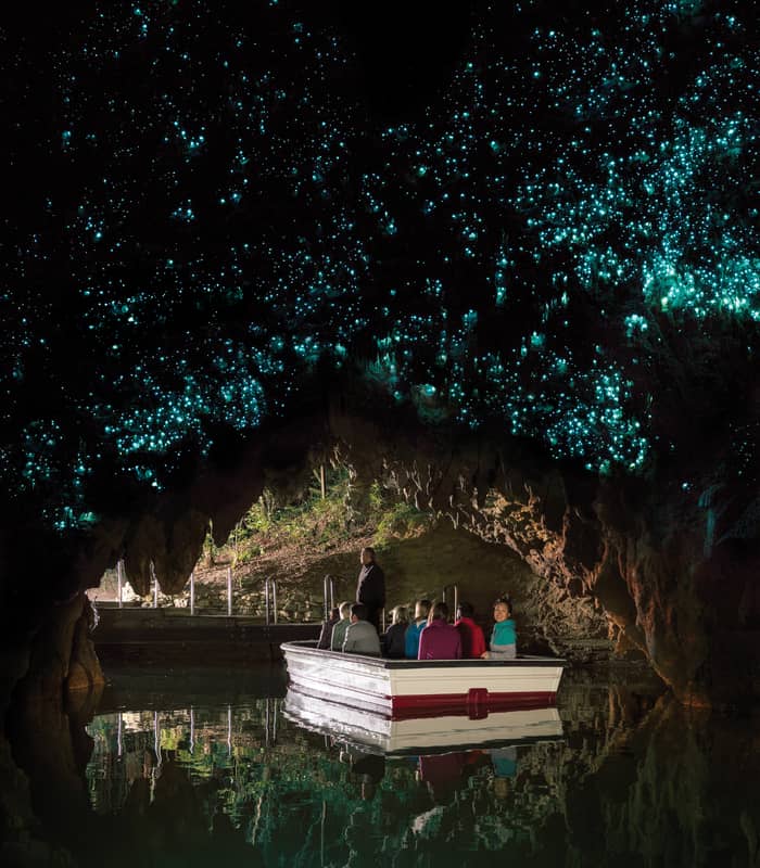 People in a boat inside Waitomo Glowworm Cave with glowing blue lights on the cave ceiling.