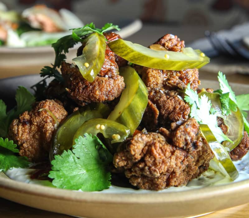 Crispy fried chicken pieces garnished with pickle slices and cilantro on a plate.