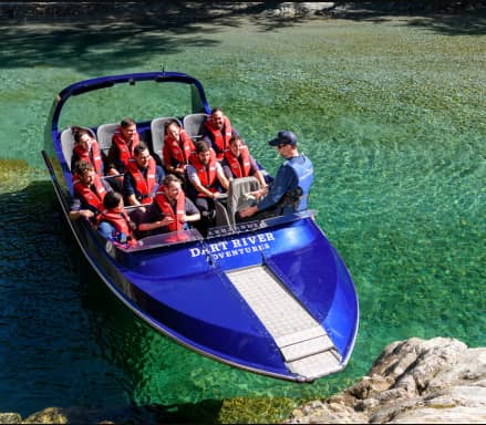 Group of people wearing life jackets on a blue jetboat in clear green river water with a guide.
