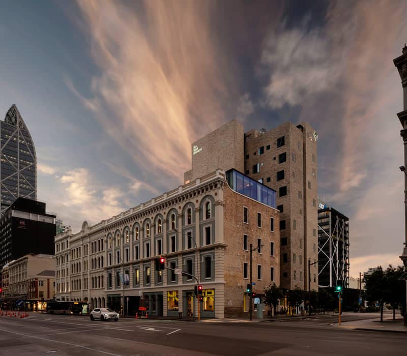 Hotel building at sunset with historic and modern architecture in a city with traffic and skyscrapers.