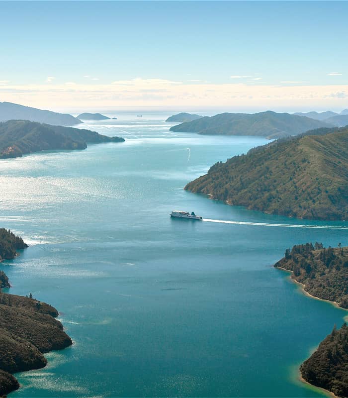 Aerial view of a ship sailing through green islands and blue waters in Marlborough Sounds.