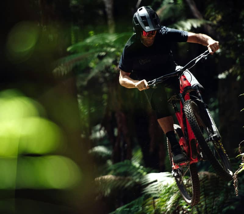 Mountain biker wearing a helmet jumping on a forest trail during daylight.