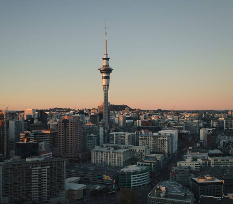 Auckland skyline with Sky Tower at sunset over city buildings and construction sites.