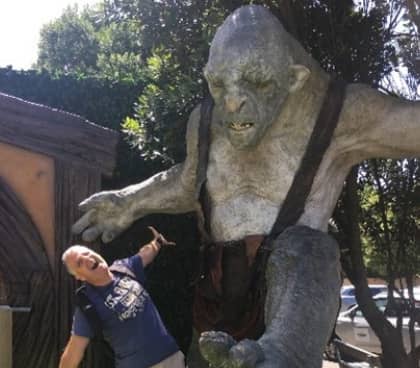 Man pretending to be attacked by a large troll statue outside in sunny weather.