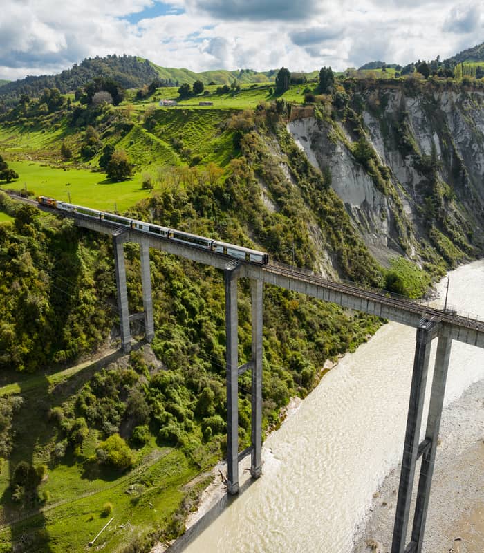 Train traveling across a high viaduct over a river surrounded by green hills and forested cliffs.